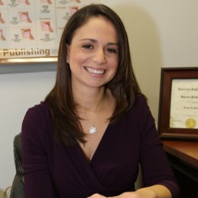 A smiling woman in a dark top and a necklace